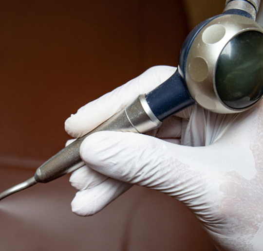 a gloved hand holding an air polisher