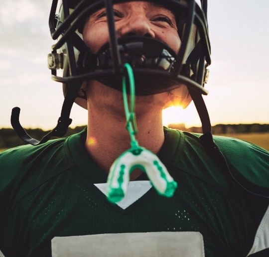 Teen with athletic mouthguard hanging from football helmet