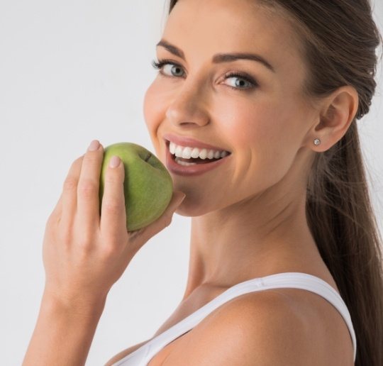 Woman eating a green apple after dental implant tooth replacement