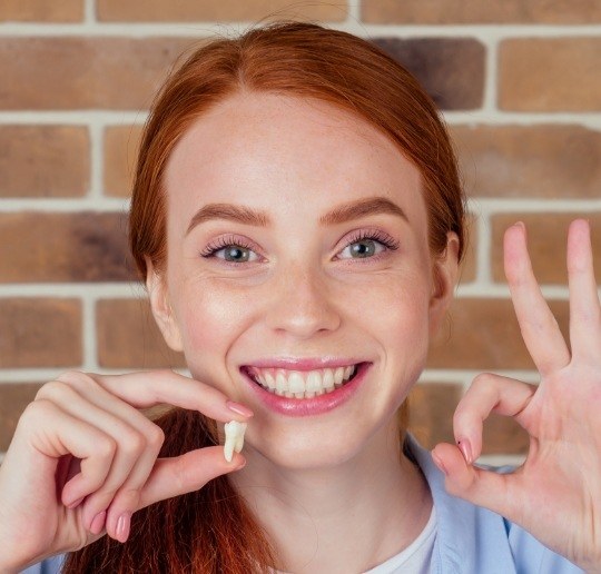 Woman holding her extracted wisdom tooth up to her face
