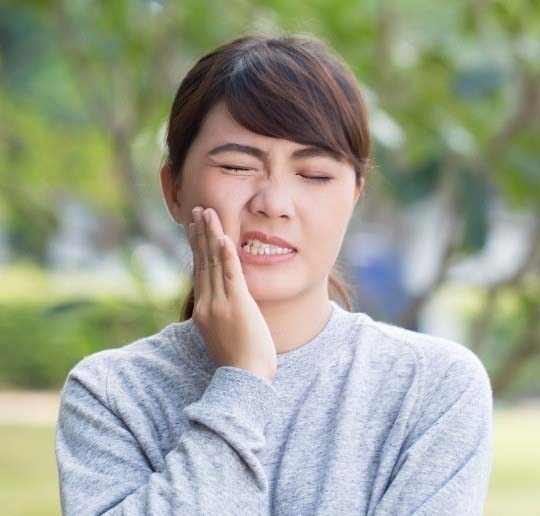 Woman in need of emergency dentistry holding cheek in pain