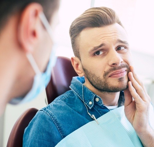 Man in need of tooth extraction holding cheek in pain