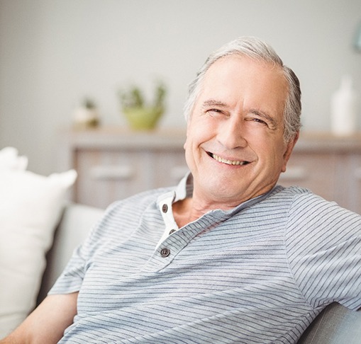 Senior man in striped shirt sitting on couch smiling