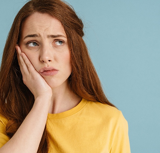 woman holding cheek in pain 