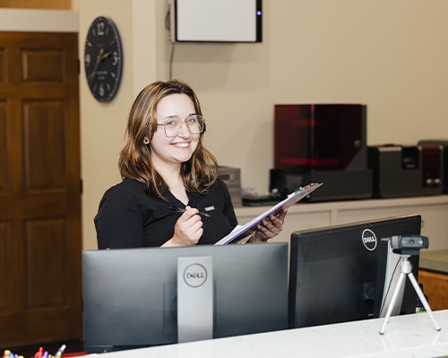 Smiling dental team member holding a clipboard at front desk