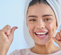 Woman smiling while flossing teeth at home