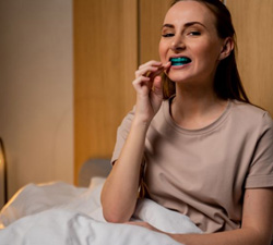 Woman sitting in bed, using oral appliance