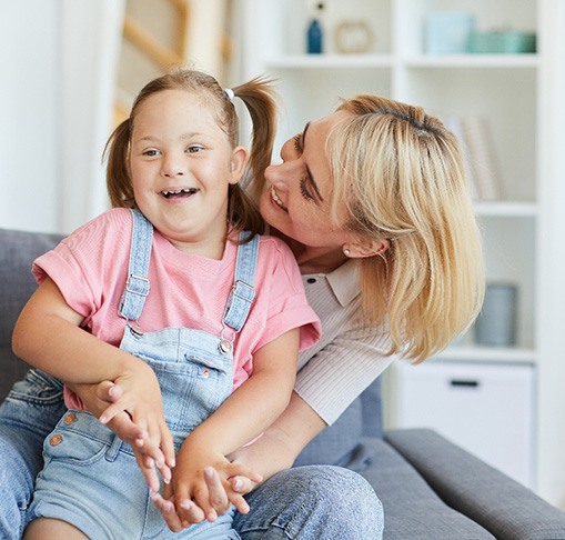 a young girl smiling and hugging her mom