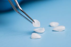 Pair of tweezers picking up a veneer form a small pile on a blue background