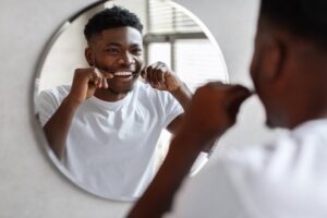 Young man flossing in front of a mirror.