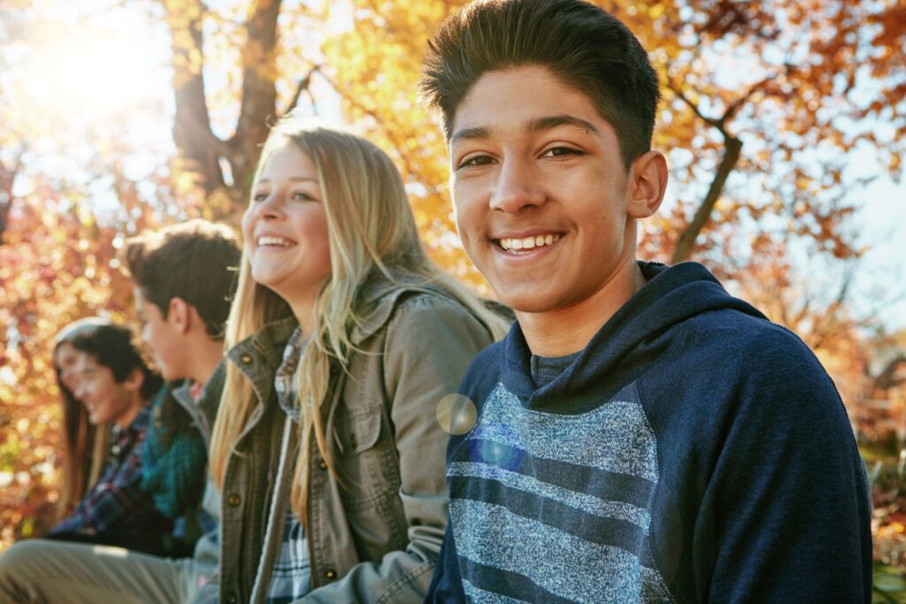 Group of teens outside under tree with orange leaves
